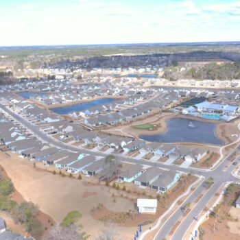 Aerial view of suburban houses, curved roads, ponds, and grass.