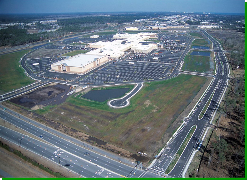 Aerial view of a mall with parking, greenery, ponds, roads.