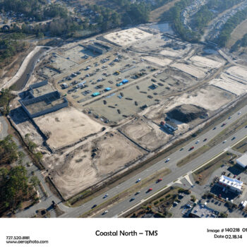 Aerial view: large cleared site, vehicles, near roads and homes.