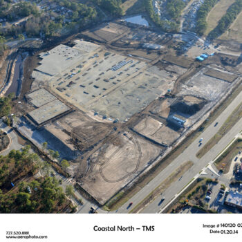 Aerial view: construction site, foundations, dirt paths, roads, homes.