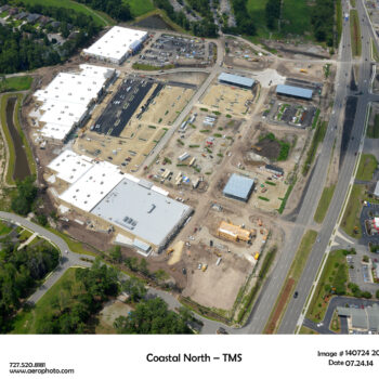 Aerial view: large construction site by road, homes, and greenery.