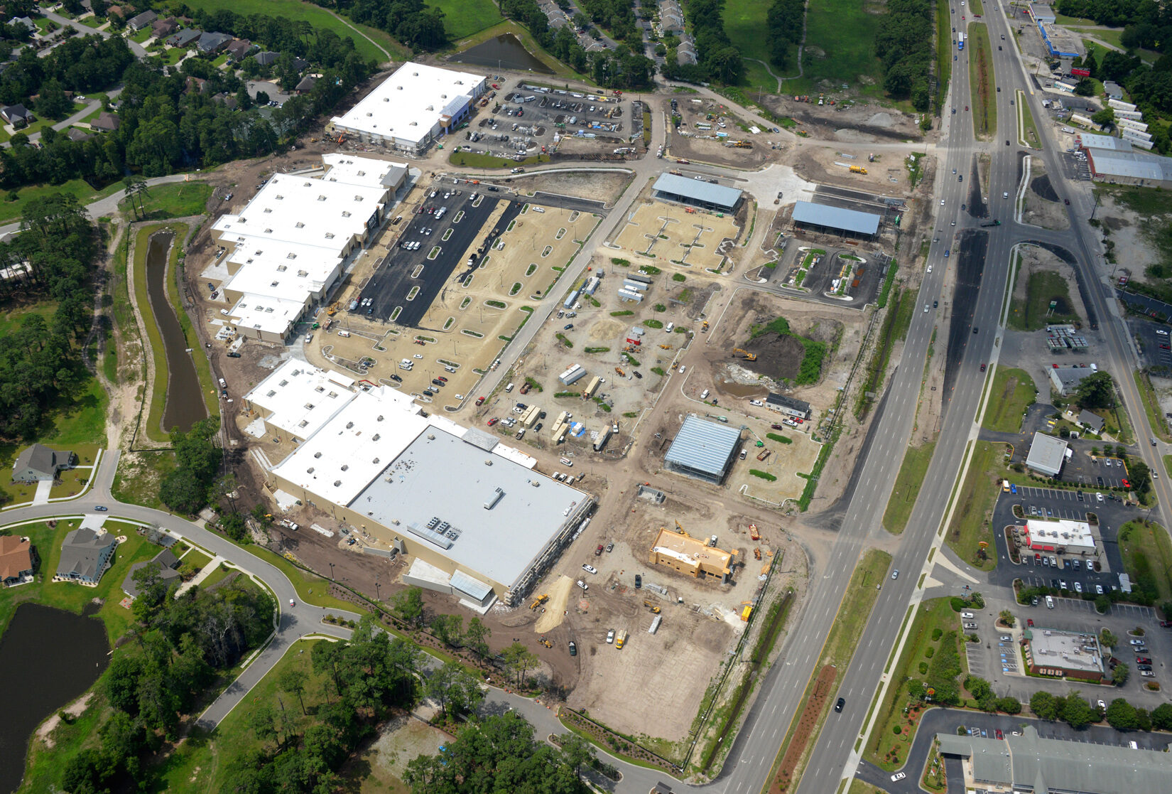 Aerial view: large construction site amid roads, homes, greenery.