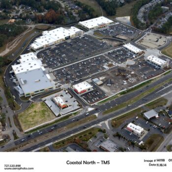 Aerial view: large shopping center, parking lots, nearby construction.