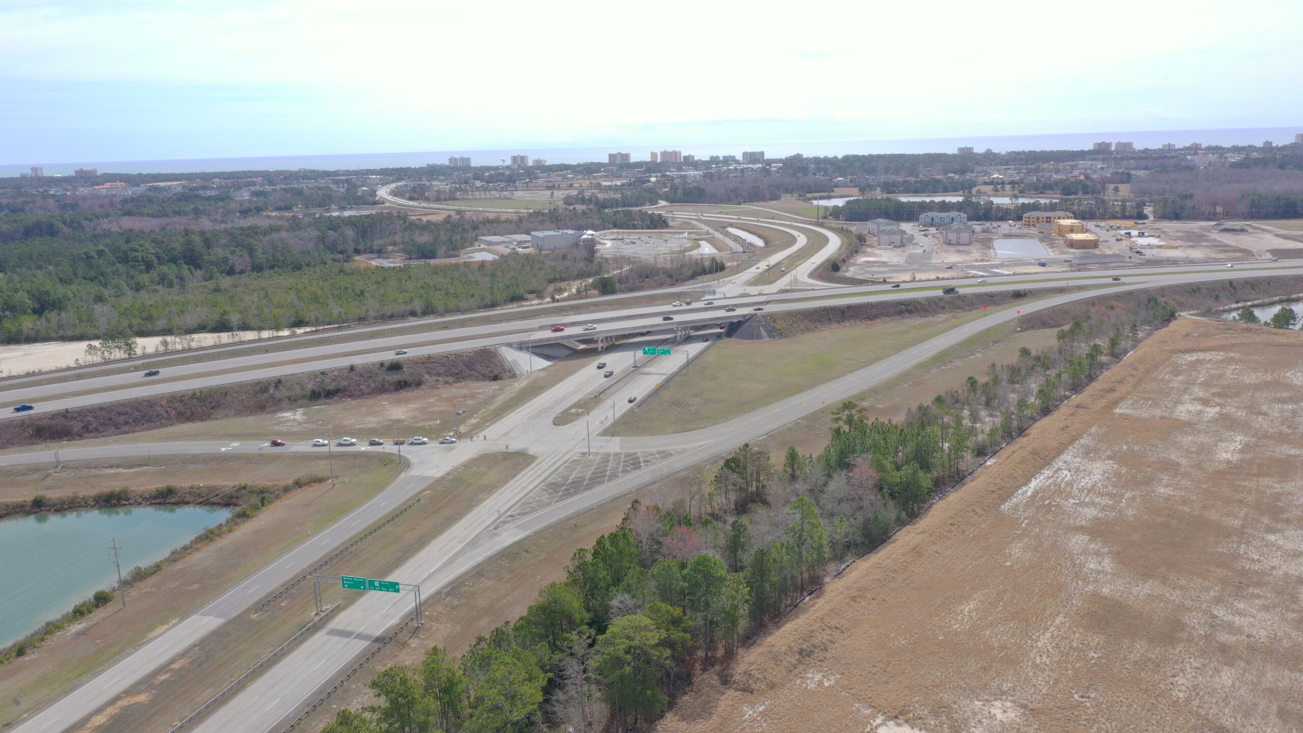 Aerial view of highway interchange amid greenery and nearby city.