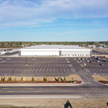 Large white industrial building, mostly empty lot, few cars.
