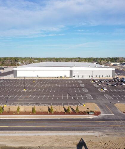 Large commercial building, few cars, mostly empty lot, blue sky.
