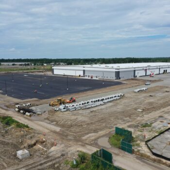 Warehouse with new lot, construction vehicles, materials, partly cloudy sky.