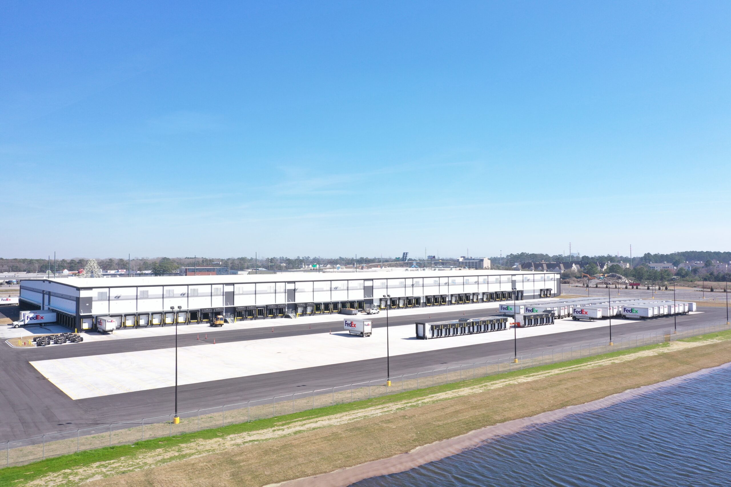 Warehouse with loading docks, trucks, pavement, and water nearby.