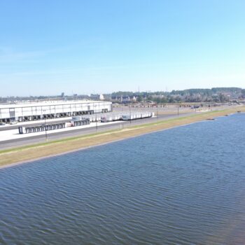 Industrial building with loading docks by wide water, clear sky.