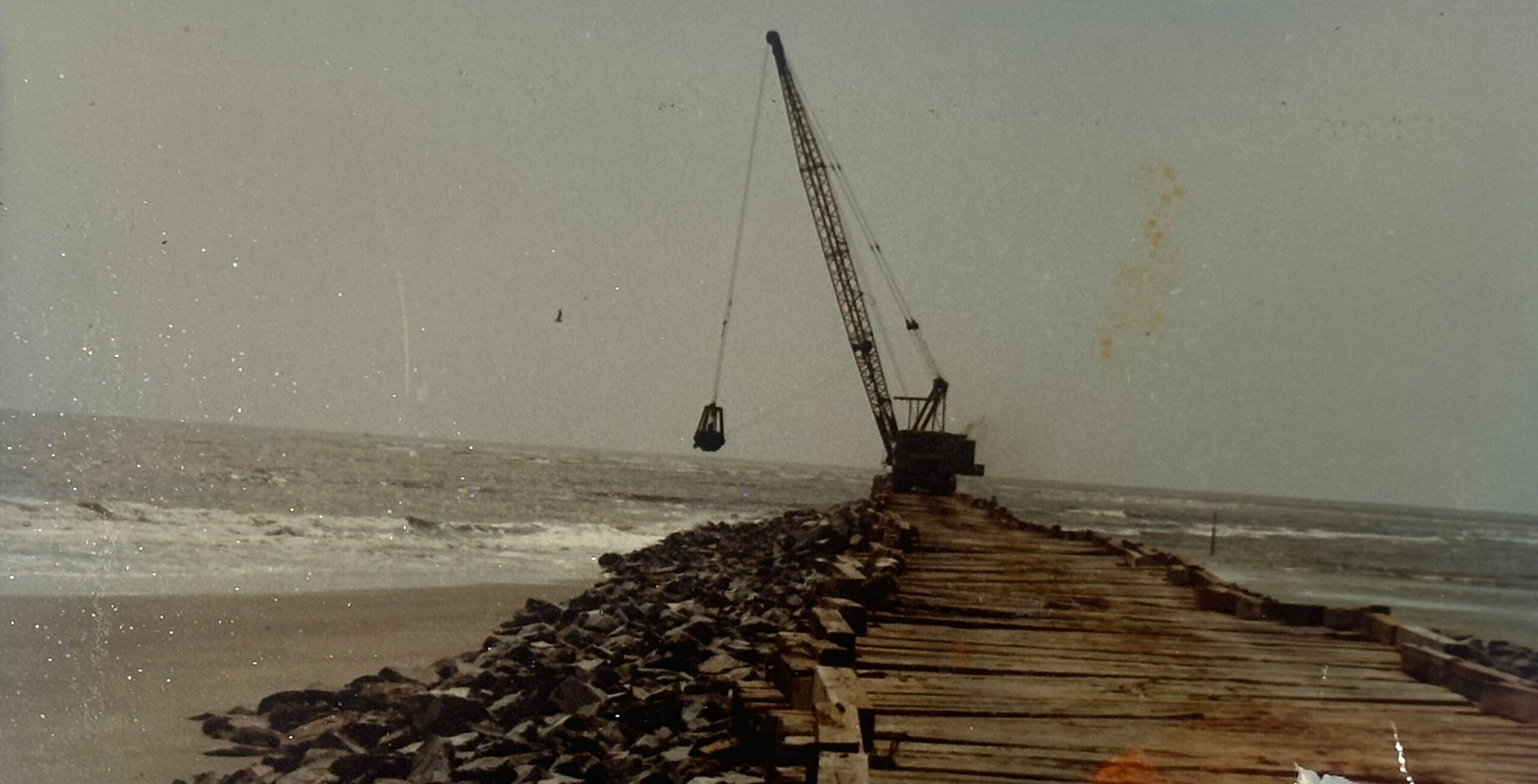 Crane on pier over rocks, stretching into the hazy ocean.