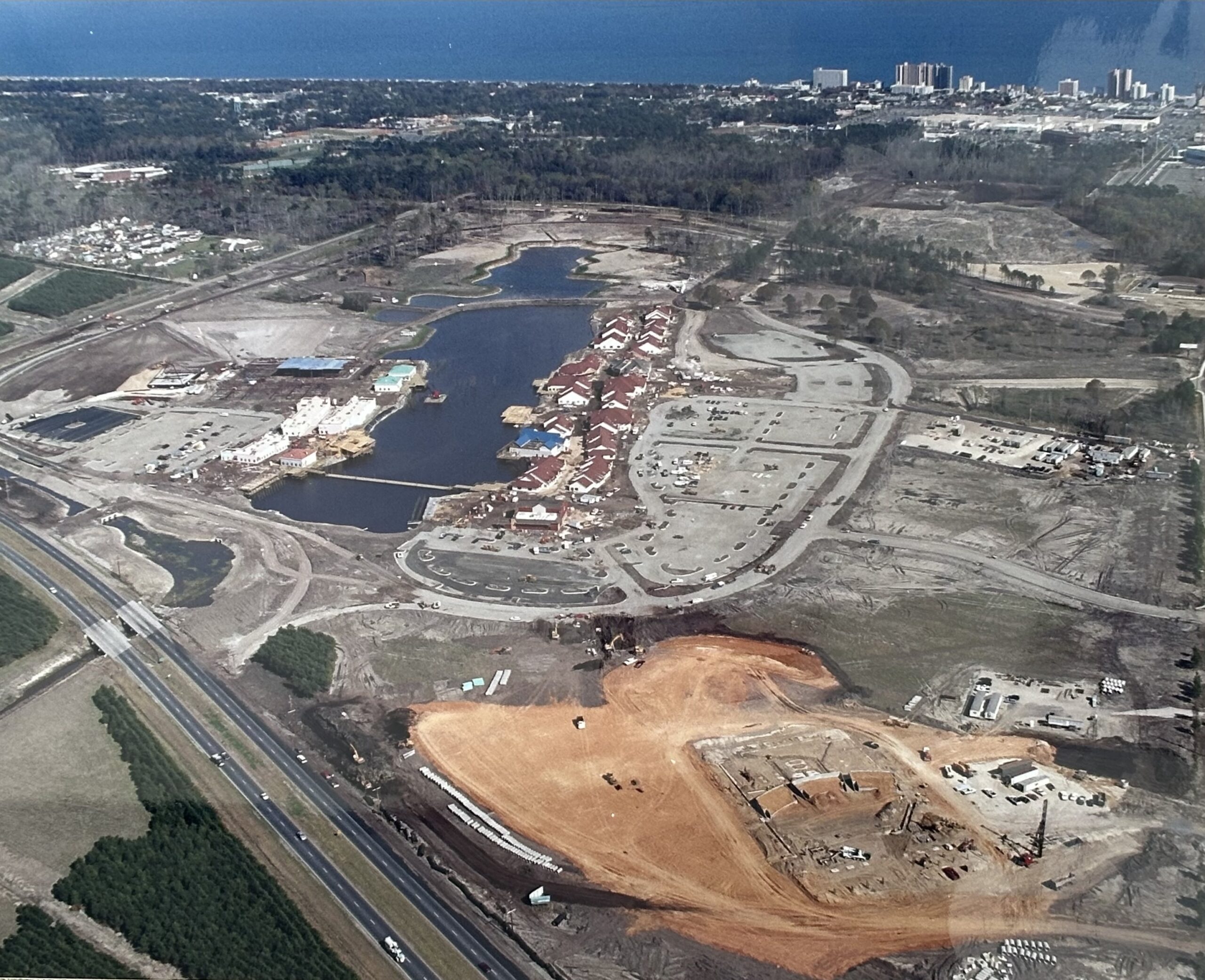 Aerial view: construction, parking lots, ponds; highway and coast.