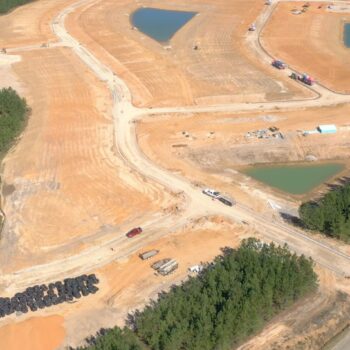 Aerial view: large construction site, dirt roads, ponds, materials.