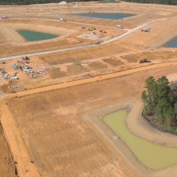 Aerial view: construction site, retention ponds, vehicles, wooded area.