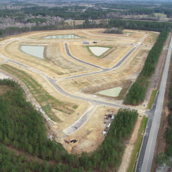 Aerial view: cleared site, roads, plots, ponds, dense forest.