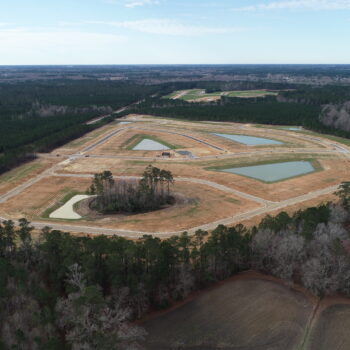 Aerial view: triangular construction site, ponds, dirt roads, forest.
