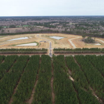 Aerial view: cleared construction site with roads, ponds, and forest.