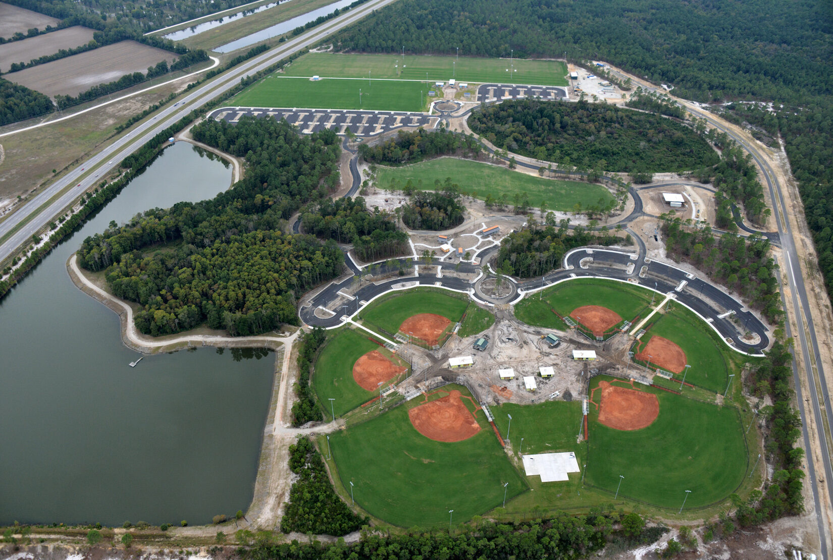 Aerial view of sports complex with fields, pond, parking, greenery.