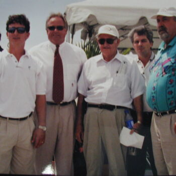 Five men pose together outside under a white tent.