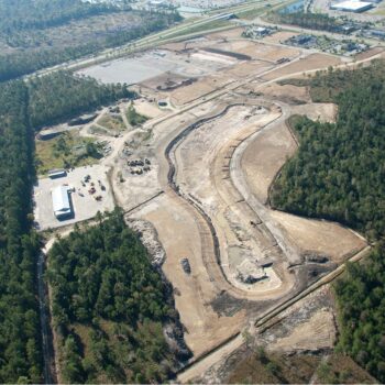 Aerial view: construction site, cleared land, machinery, forest nearby.