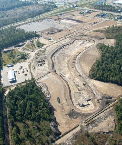 Aerial view: construction site, cleared land, machinery, forest nearby.
