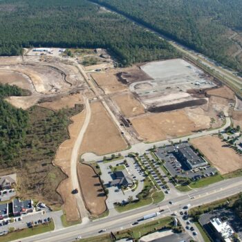 Aerial view: construction site, cleared land, buildings, roads, forest.