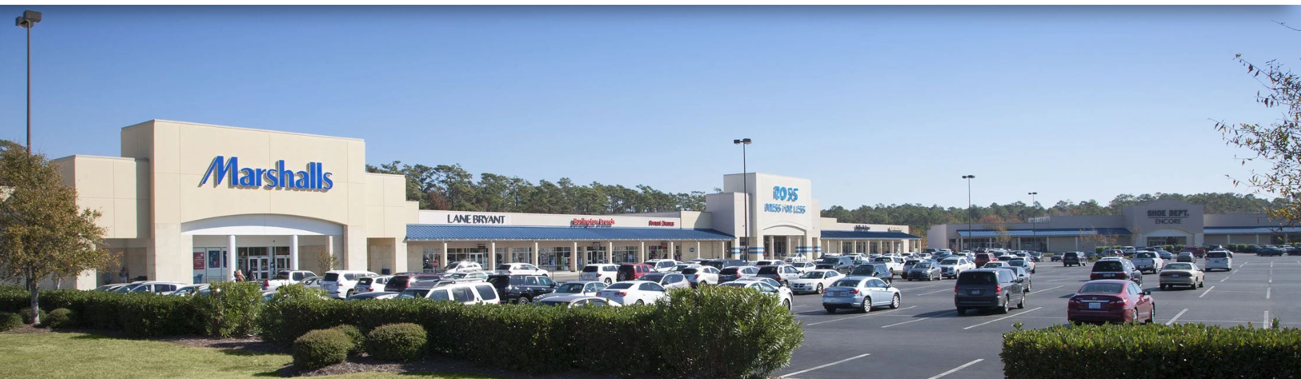 Shopping center lot with cars, Marshalls, gym, and shops.