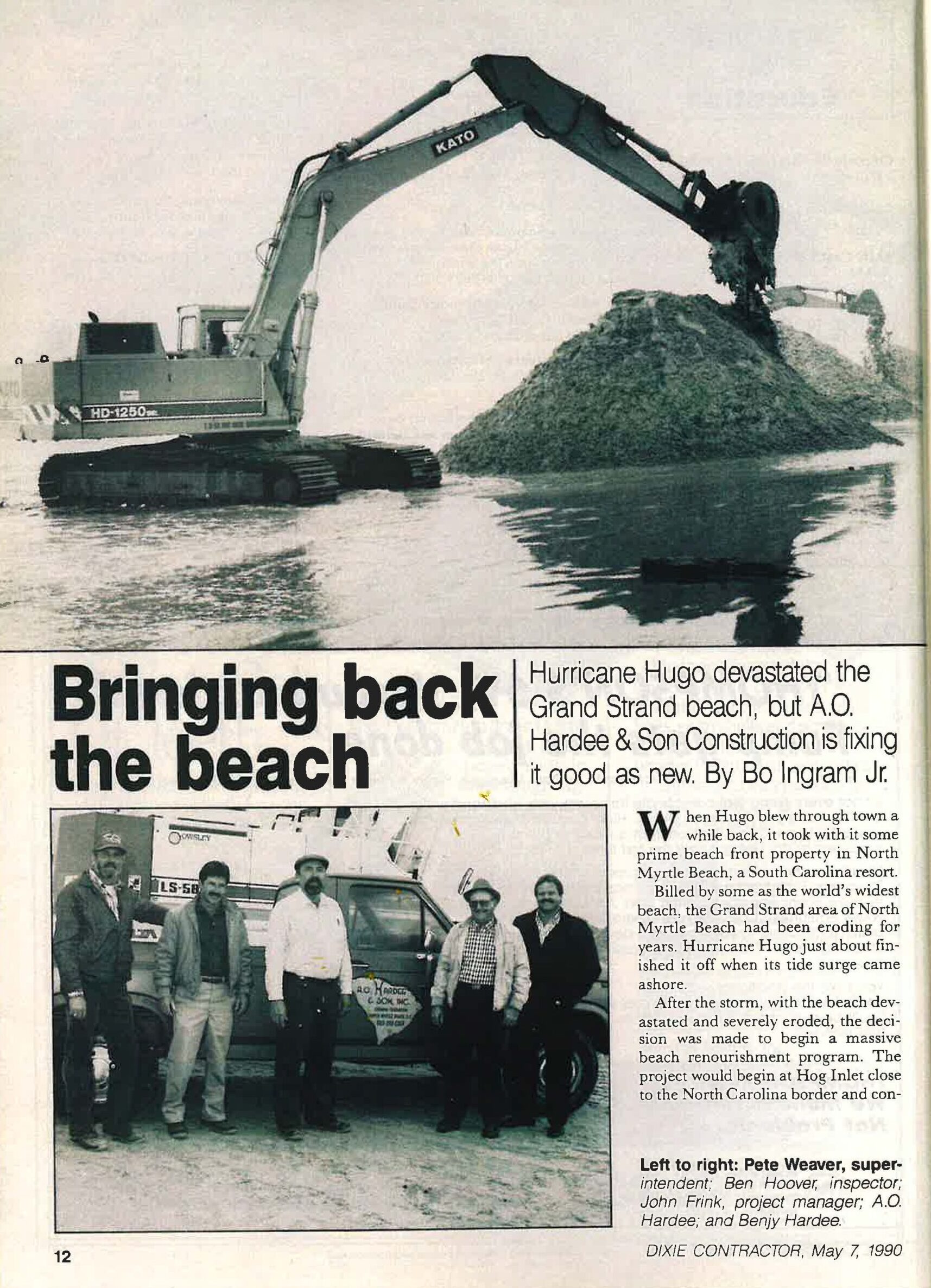 Excavator moves sand; five men stand by construction truck.