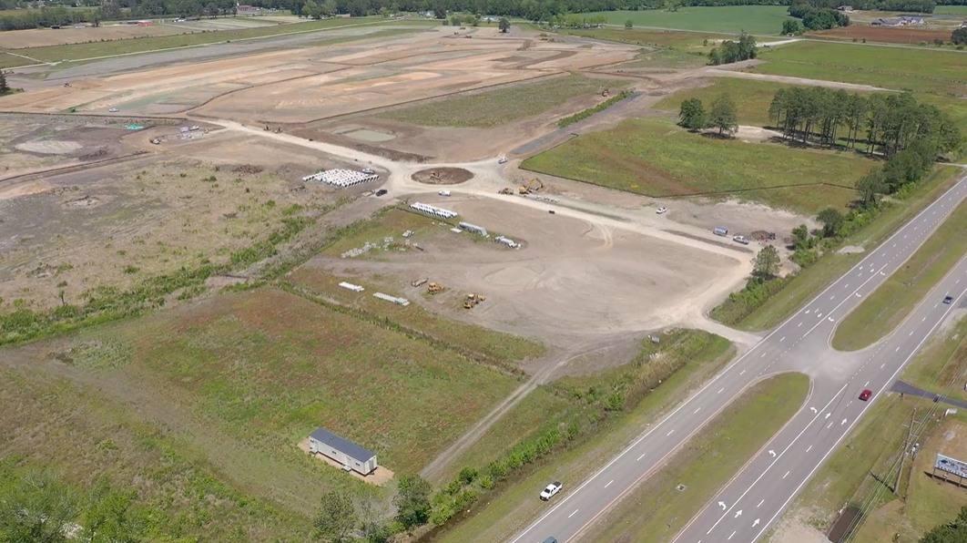 Aerial view: cleared construction site, equipment, nearby road, some trees.