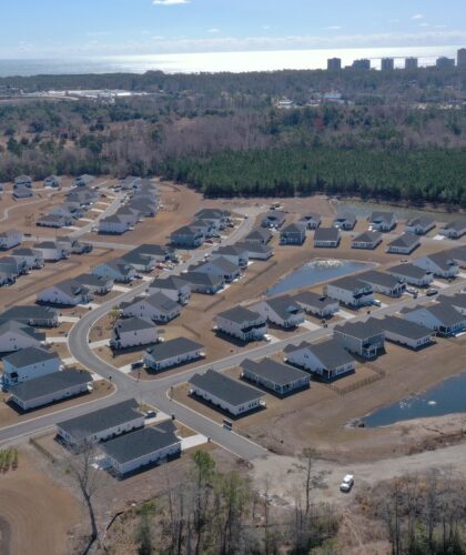 Aerial of suburb: houses, curving streets, ponds, forest, distant city.