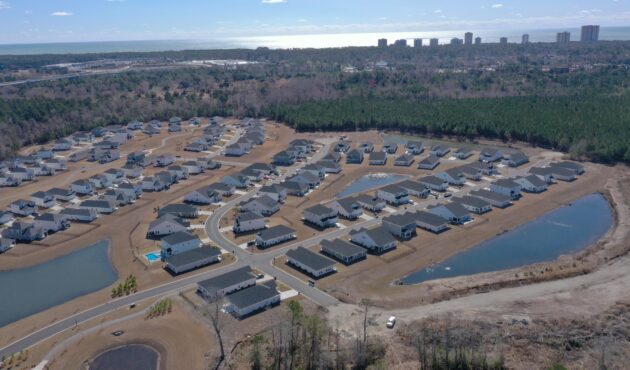 Aerial of suburb: houses, curving streets, ponds, forest, distant city.