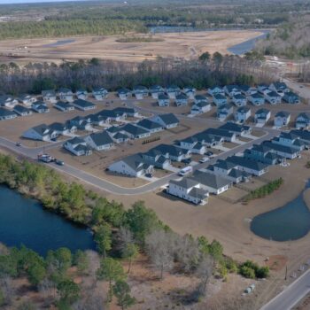 Aerial view of suburb: houses, roads, pond, and woods.