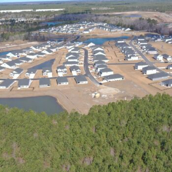 Aerial view: suburban homes and roads under construction, trees nearby.