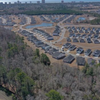 Aerial of suburban homes on curving streets amid trees and water.