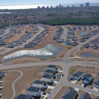 Aerial view of suburb: houses, curved streets, ponds, woods.