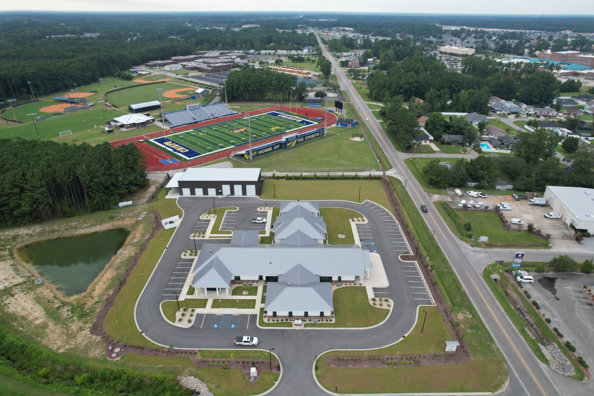 Aerial view: school campus, sports fields, parking, trees, houses.