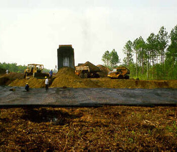 Construction vehicles and workers grade soil as truck unloads dirt.