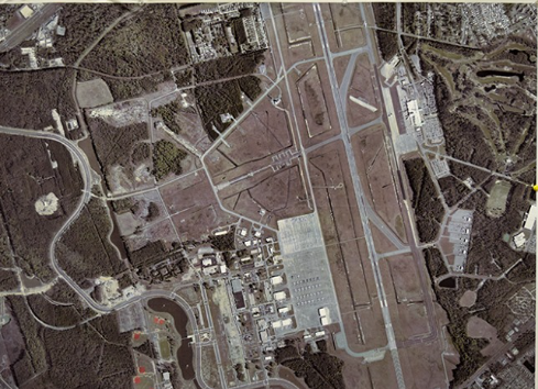 Aerial view of airport, runways, buildings, and wooded area.