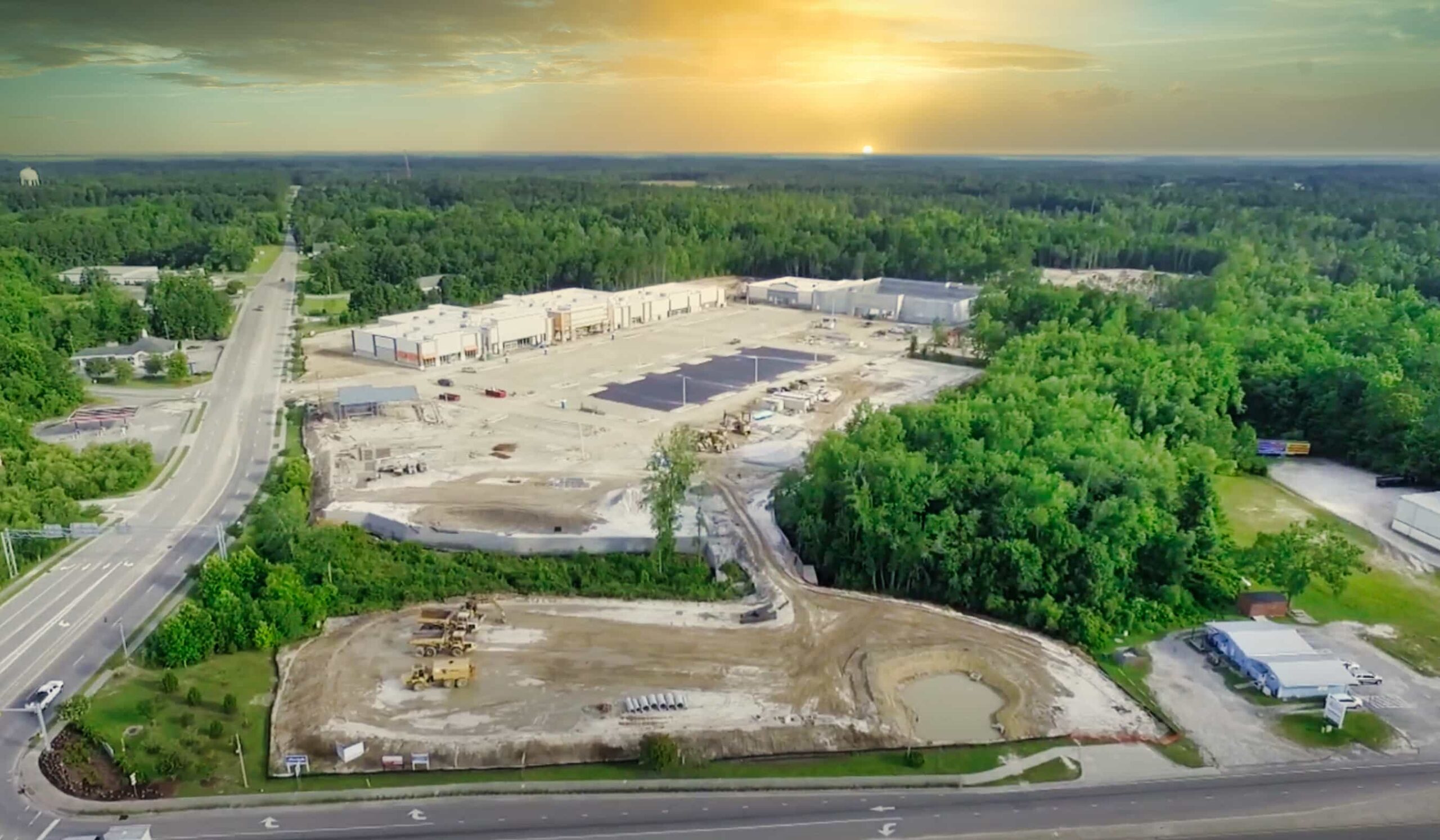 Aerial sunset view: construction site, large buildings, trees, roads.
