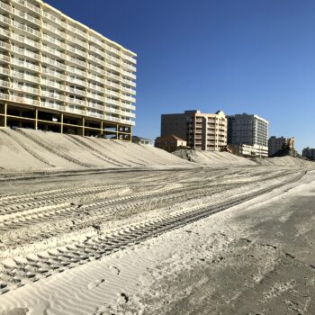Tall beachfront buildings overlook wide sandy beach with tire tracks.