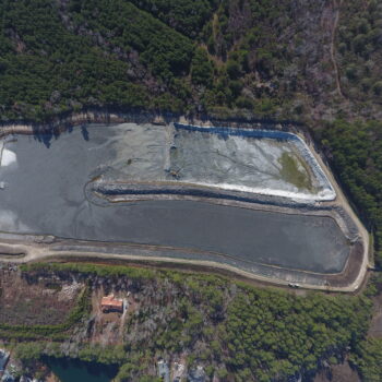 Aerial view: rectangular pond, trees, dirt road, nearby buildings.