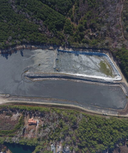 Aerial view: rectangular pond, trees, dirt road, nearby buildings.